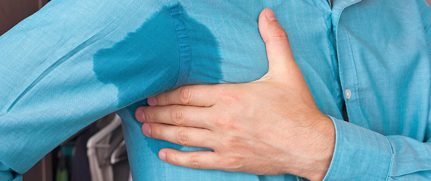 Imagem de uma pessoa usando uma camisa azul onde esta molhada de suor abaixo das axilas, representando a hiperidrose axiliar