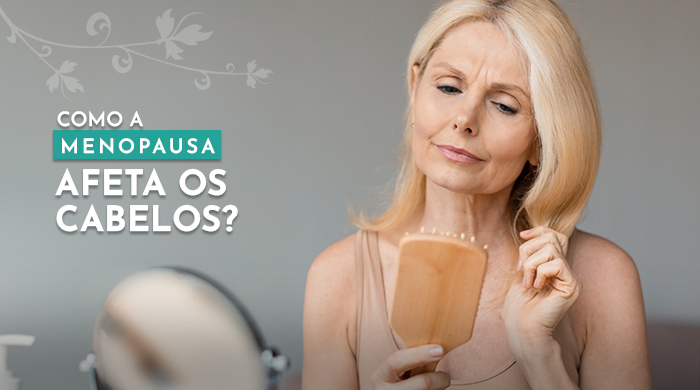 A imagem mostra um mulher loira de meia-idade olhando preocupada para uma escova de cabelo em suas mãos, refletindo os efeitos da menopausa na saúde dos cabelos.