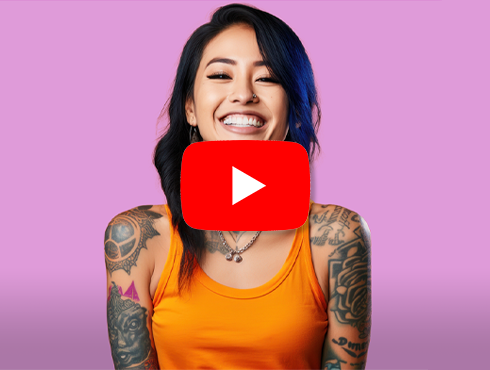 Mulher sorridente com cabelos escuros e várias tatuagens nos braços, vestindo uma blusa laranja, com o ícone do YouTube sobreposto ao centro da imagem. Fundo rosa claro.